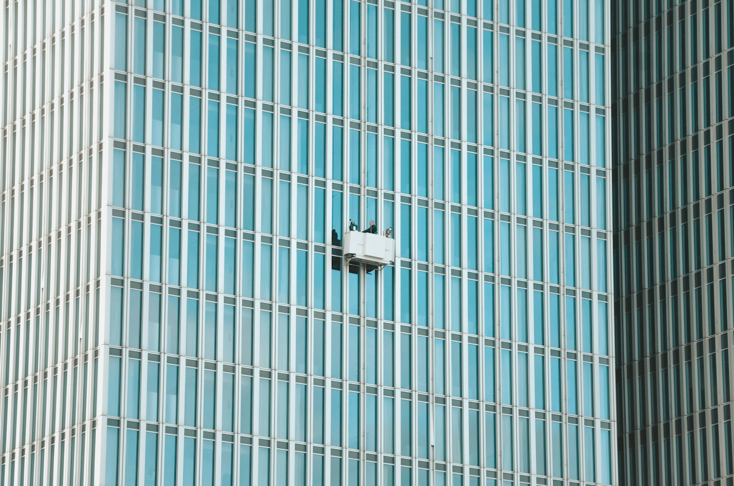 Arbeiter auf einer Arbeitsbühne reinigen die Fenster eines modernen Bürogebäudes.