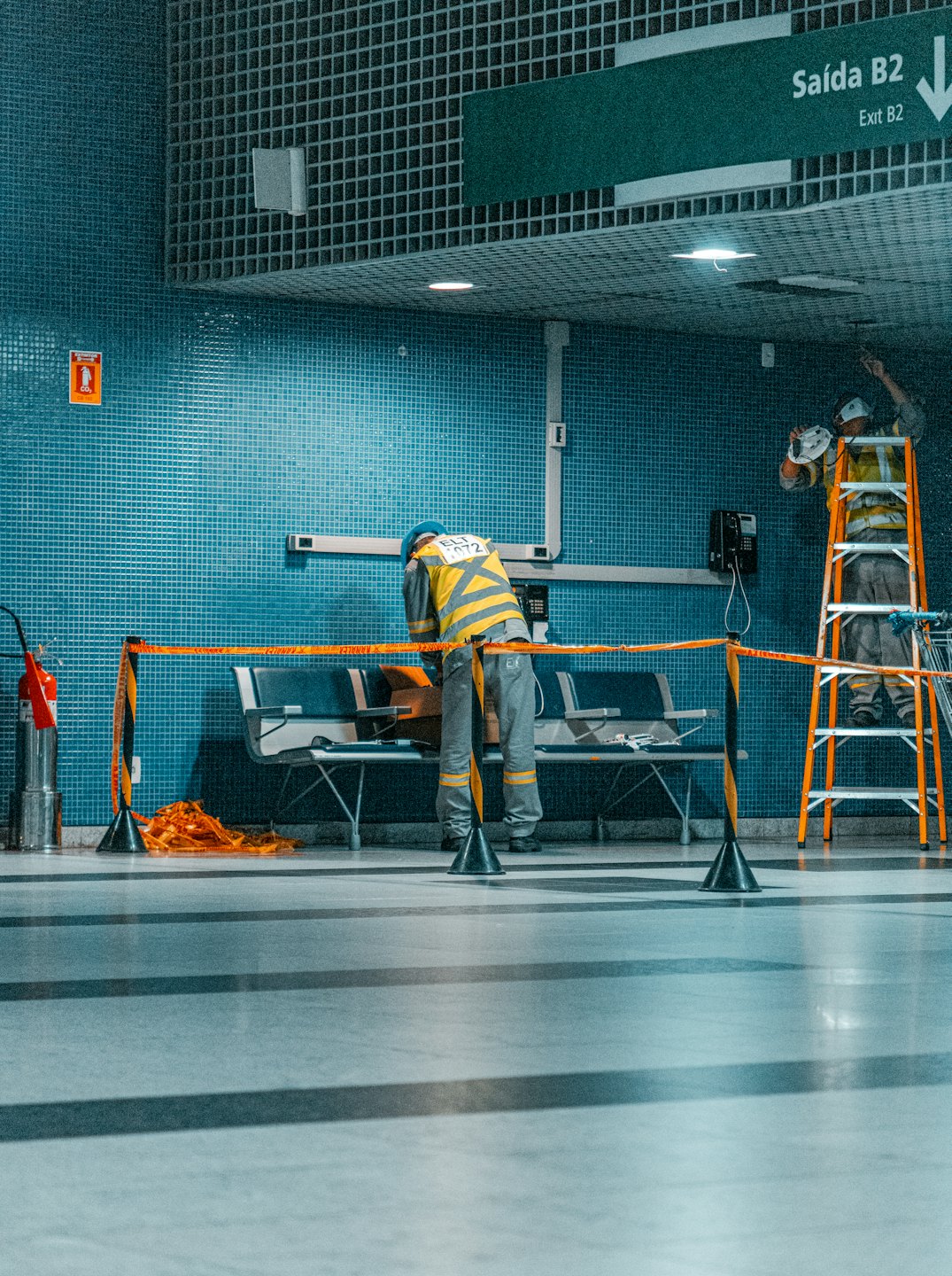 Arbeiter in Schutzkleidung warten Armaturen in einem gefliesten öffentlichen Gebäude.